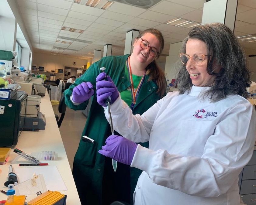 LBCUK Trustee Helen Coulthard, wearing a white lab coat, is being shown lab techniques by researcher Esme Bullock.
