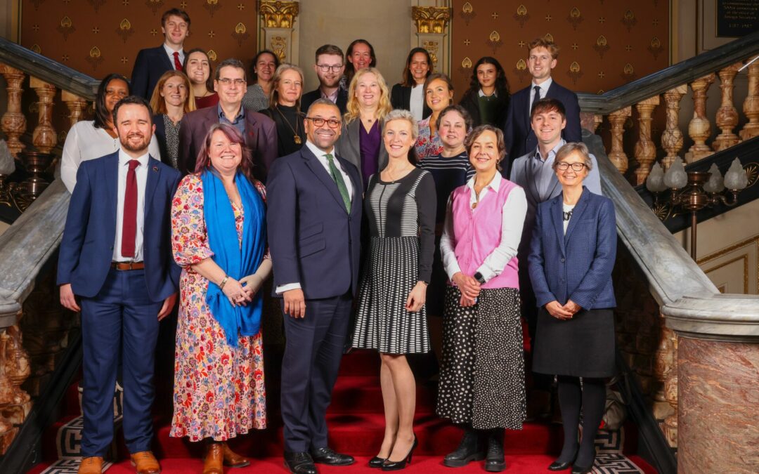 UK Foreign Secretary James Cleverly and his wife Susie stand on stairs with 20 Civil Servants from the Foreign Office to demonstrate the 22 people diagnosed every day with Lobular Breast Cancer